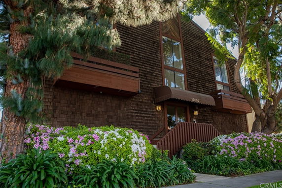 Front view of a multi-story building with wooden exterior and shrubs in front.