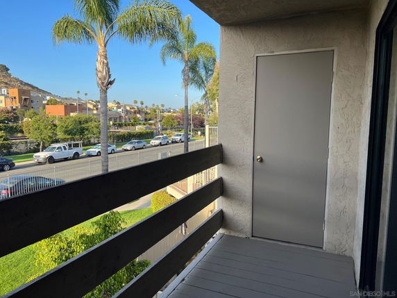 View from a balcony overlooking a street with cars and palm trees.