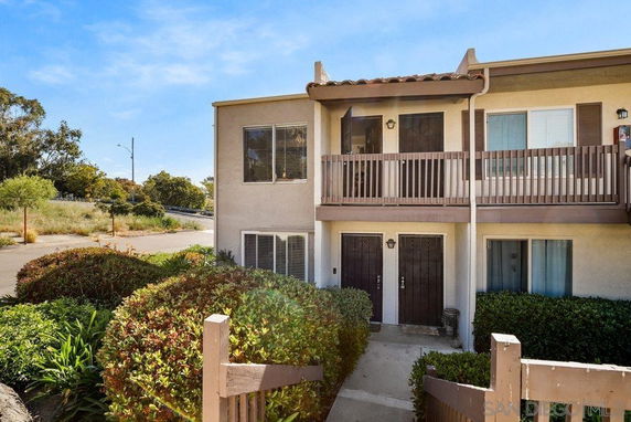 Front view of a two-story townhouse with balconies and shrubs in front.