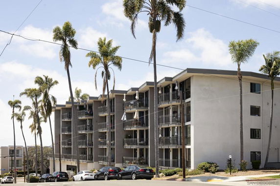 Front view of a multi-story apartment building with balconies and palm trees.