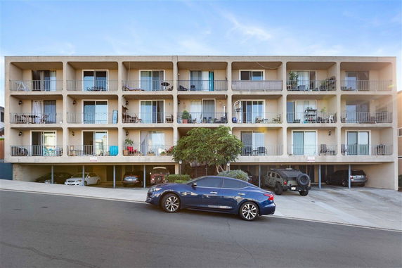 Front view of a multi-story apartment building with balconies and parking area underneath.