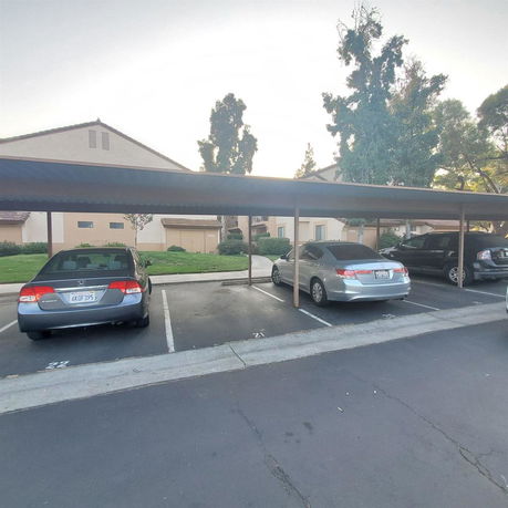 Outdoor covered parking area with several cars parked under a canopy.