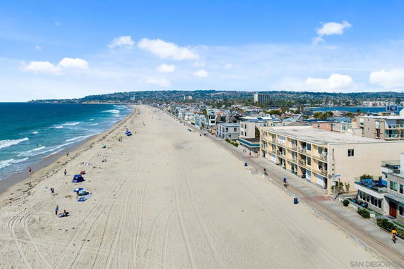 Aerial view of beachfront buildings adjacent to a long sandy beach and ocean waves.
