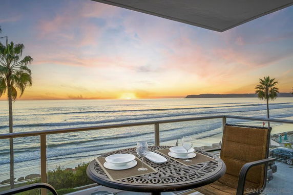 Balcony view overlooking ocean at sunset with table and chairs.