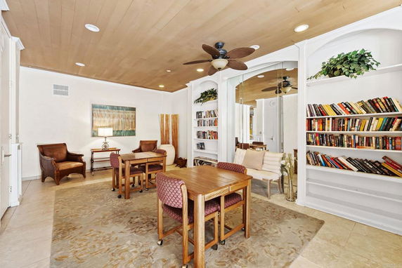 Indoor room with bookshelves, tables, chairs, and ceiling fan.
