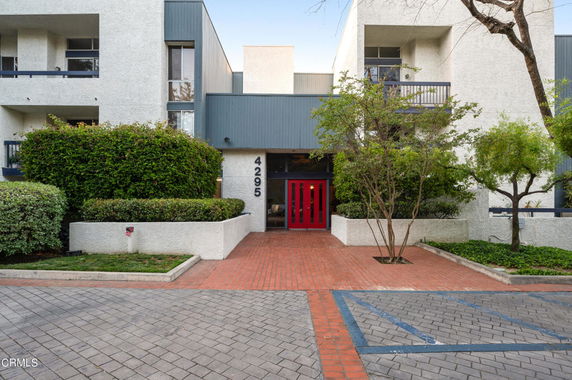 Front view of a multi-story building with balconies and a red door entrance.