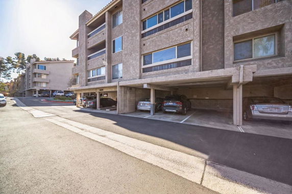 Outdoor parking area with covered parking spaces in front of a multi-story building.
