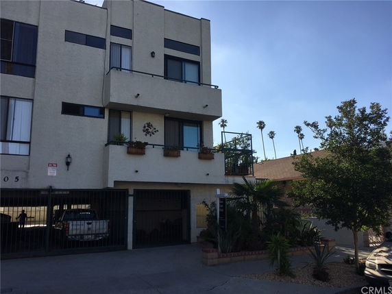Front view of a multi-story building with balconies and parking area below.