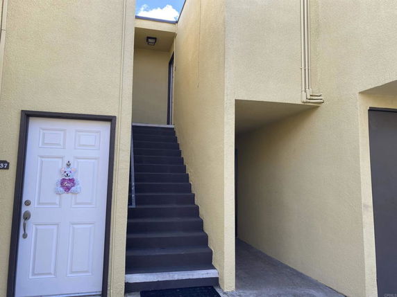 Entrance view of a building with stairs leading to the upper floor and a door on the ground level.