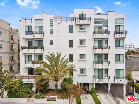 Front view of a multi-story residential building with multiple balconies and large windows.