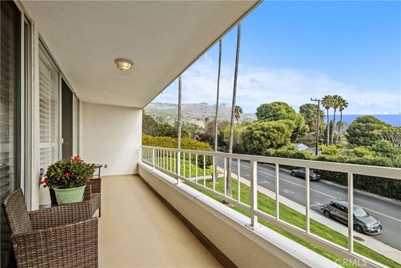 Balcony with railing and outdoor furniture overlooking trees and a street.
