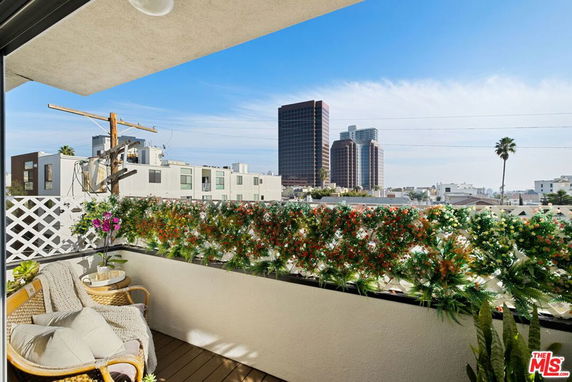 View from a balcony overlooking surrounding buildings with foliage and seating area.