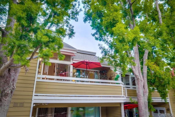 Front view of a multi-story house with a balcony and a red umbrella.