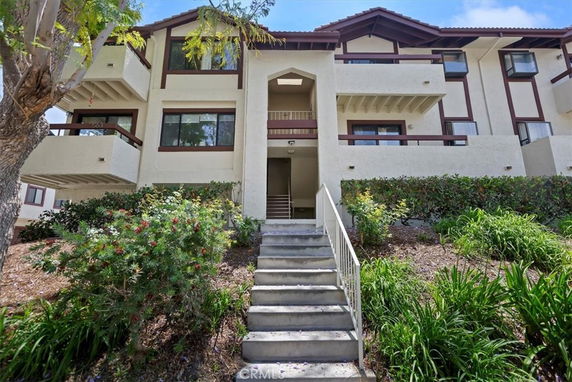 Front view of a multi-story residential building with balconies and a staircase leading to the entrance.