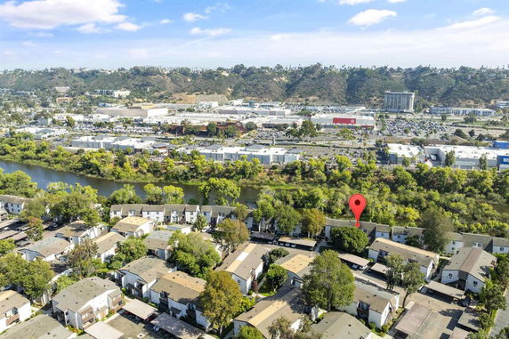 Aerial view showing residential houses with a backdrop of a river, trees, and a distant commercial area.
