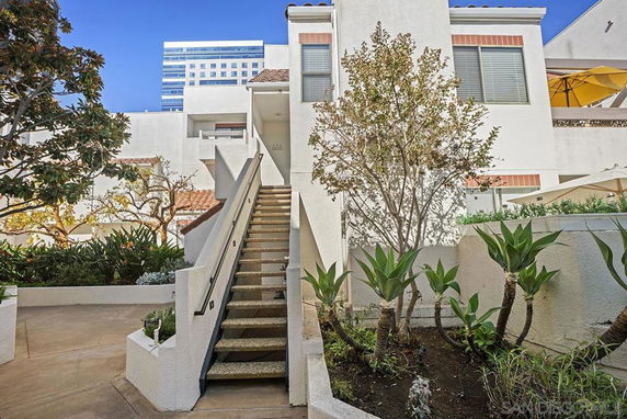 Front view of a multi-story building with an external staircase and surrounding vegetation.