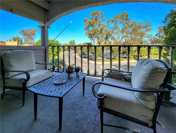 View from a balcony with outdoor seating and a table, showing the neighborhood and trees in the background.