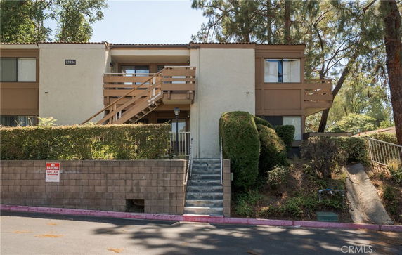 Front view of a two-story residential building with wooden balcony and exterior staircase.