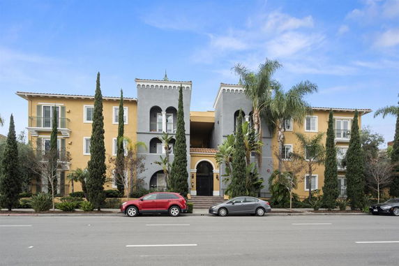 Front view of a multi-story apartment building with a central archway entrance and palm trees.