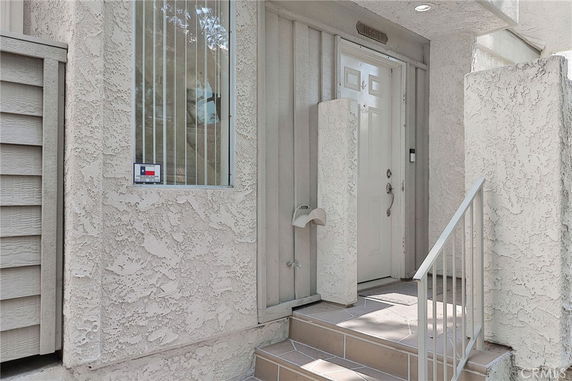 Front view of an entrance door with surrounding stucco walls and a small staircase.
