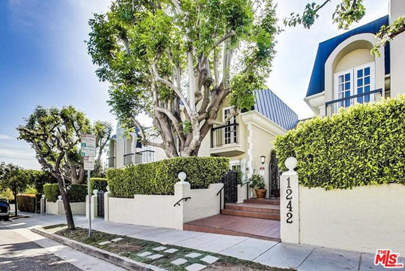 Front view of a multi-story house with hedges and large trees.