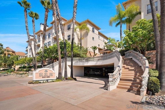 Front view of a multi-story residential building with a curved staircase and palm trees.
