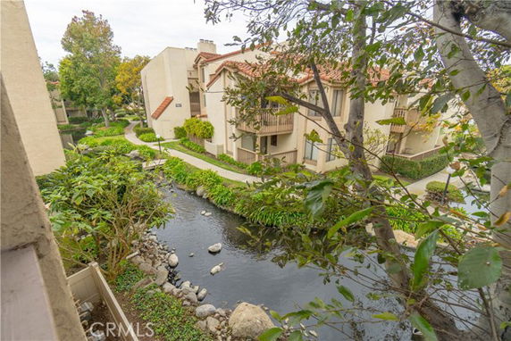 View of multi-story residential buildings with balconies, surrounded by landscaped pathways and a creek.