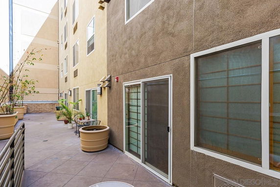 View of a multi-story building exterior with large windows and sliding doors leading to a patio area.