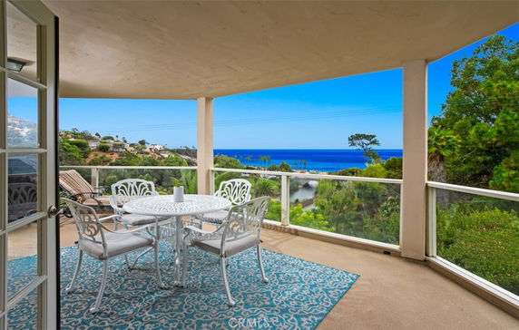 Outdoor balcony with a table and chairs, offering a panoramic view of the ocean and surrounding landscape.