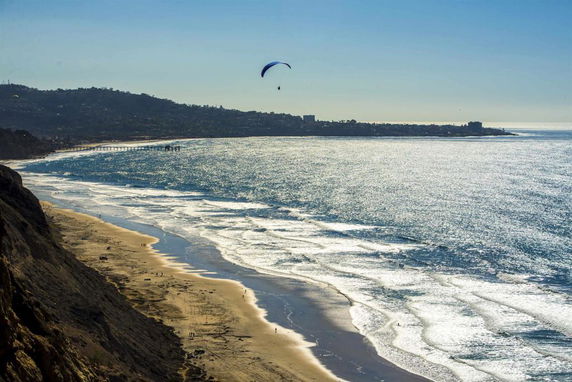 Panoramic view of a coastline with a beach and a paraglider in the sky.
