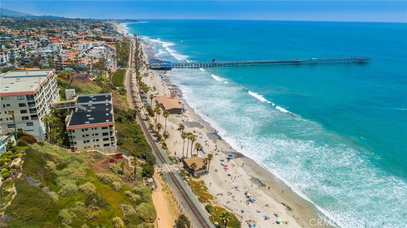 Aerial view of beachfront buildings adjacent to a coastline with a long pier extending into the ocean.