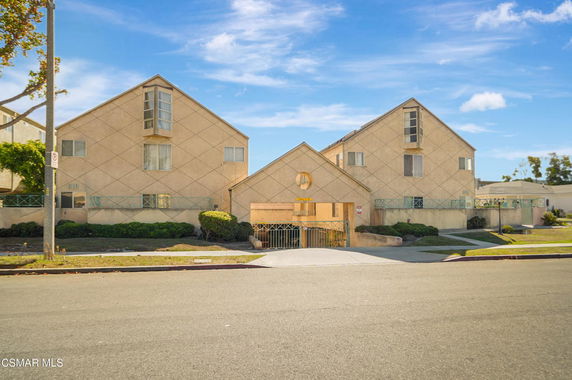 Front view of a multi-story building with triangular roof sections and gated entrance.