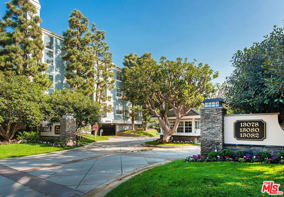 Front view of a multi-story residential building with trees and a driveway.