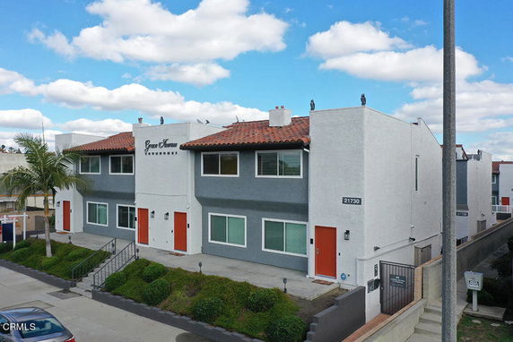 Front view of a two-story townhouse building with red doors and a gray and white exterior.