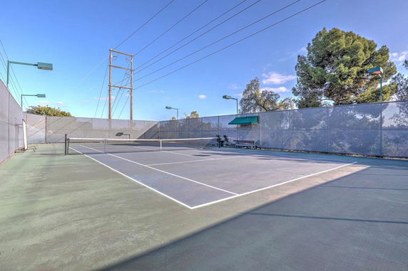 Outdoor tennis court with surrounding fence and nets.