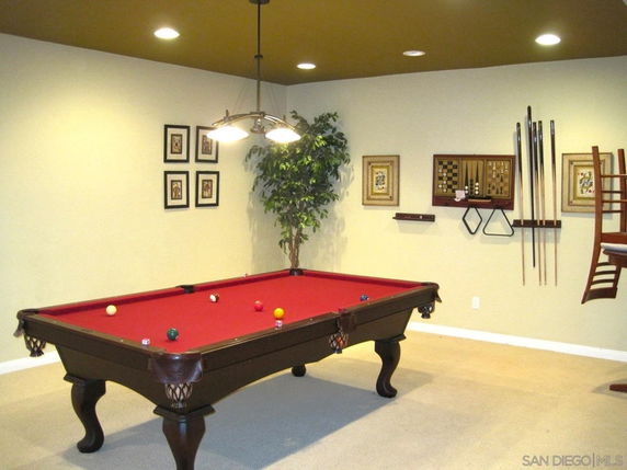 Room with a red-felt billiards table and wall-mounted billiard cues.
