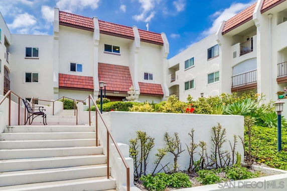 Front view of a multi-story apartment building with red-tiled roof accents and stairway leading to entrance.
