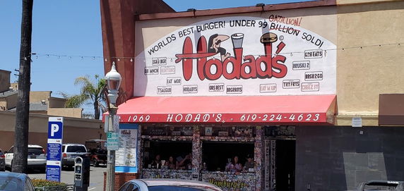 Front view of a restaurant with a large sign advertising burgers.
