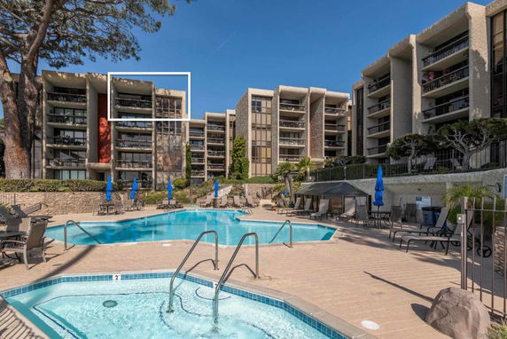 View of an apartment complex with outdoor swimming pool and sun loungers.
