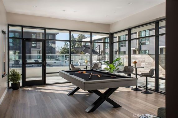 Indoor area with a pool table and seating, featuring large windows overlooking an outdoor patio.