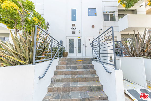 Front view of a modern multi-story building with stairs leading to the entrance.