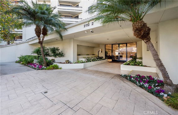 Front view of a building entrance with a covered walkway and surrounding plants.
