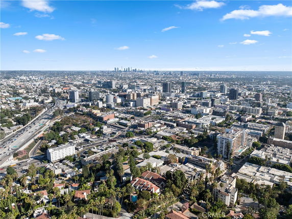 Aerial panoramic view of a city with numerous buildings and a highway, under a clear blue sky.