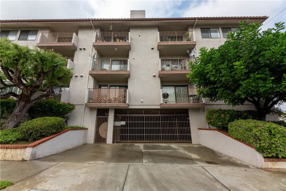 Front view of a multi-story residential building with balconies and a gated entrance at the ground level.