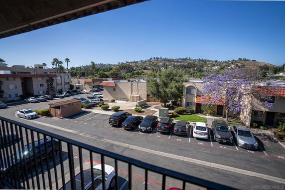 View from a building overlooking an apartment complex and parking area with hills in the background.