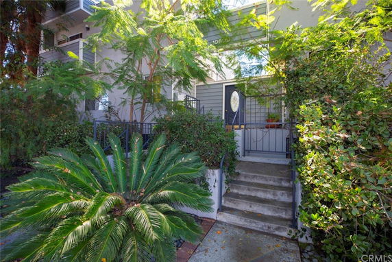 Front view of a house with greenery and a staircase leading to the entrance.