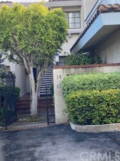 Front view of a house with a staircase leading to the entrance and a surrounding hedge.