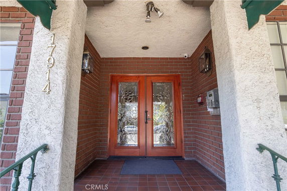 Front entrance of a building with decorative glass double doors and brick walls.