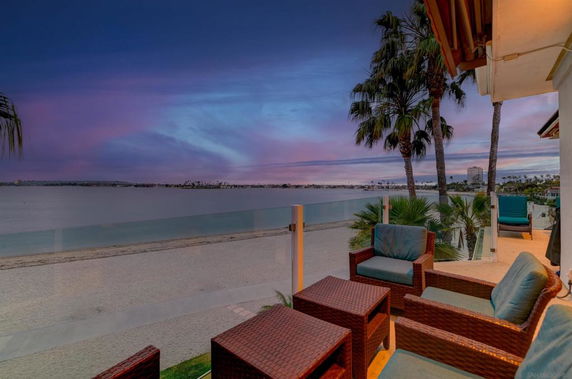 Panoramic view from a balcony overlooking a beach and ocean with palm trees and seating area.