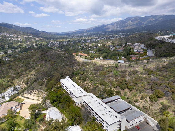 Wide-angle view of a building situated in a hilly, residential area with surrounding greenery and distant mountains.